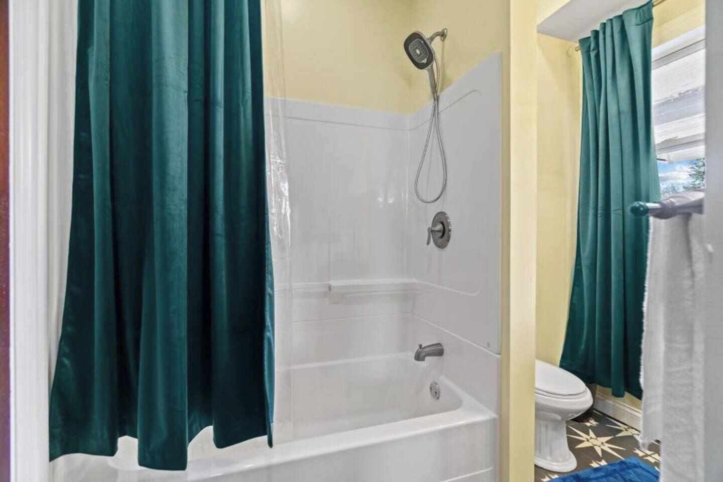 Un baño con bañera, ducha, inodoro y cortinas verdes.