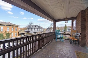 Un balcon en bois avec une balustrade, une chaise à bascule bleue et un banc en bois.