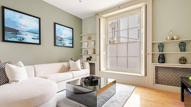 Un salón moderno con un sofá blanco, una mesa de centro de cristal y un ventanal con vistas a un edificio.