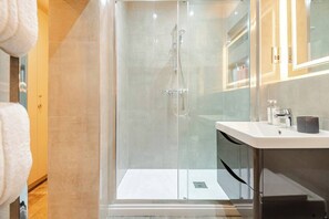 Ein modernes Badezimmer mit einer begehbaren Glasdusche, einem weißen Waschbecken und einem Spiegel darüber.