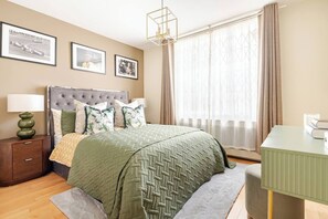 Ein ordentlich eingerichtetes Schlafzimmer mit einem gepolsterten Kopfteil, einer grün gesteppten Bettdecke und einem Nachttisch mit einer Lampe.