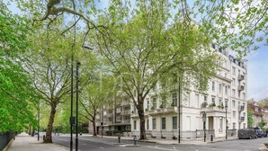 Una calle bordeada de árboles con una hilera de edificios blancos, una acera y una carretera.