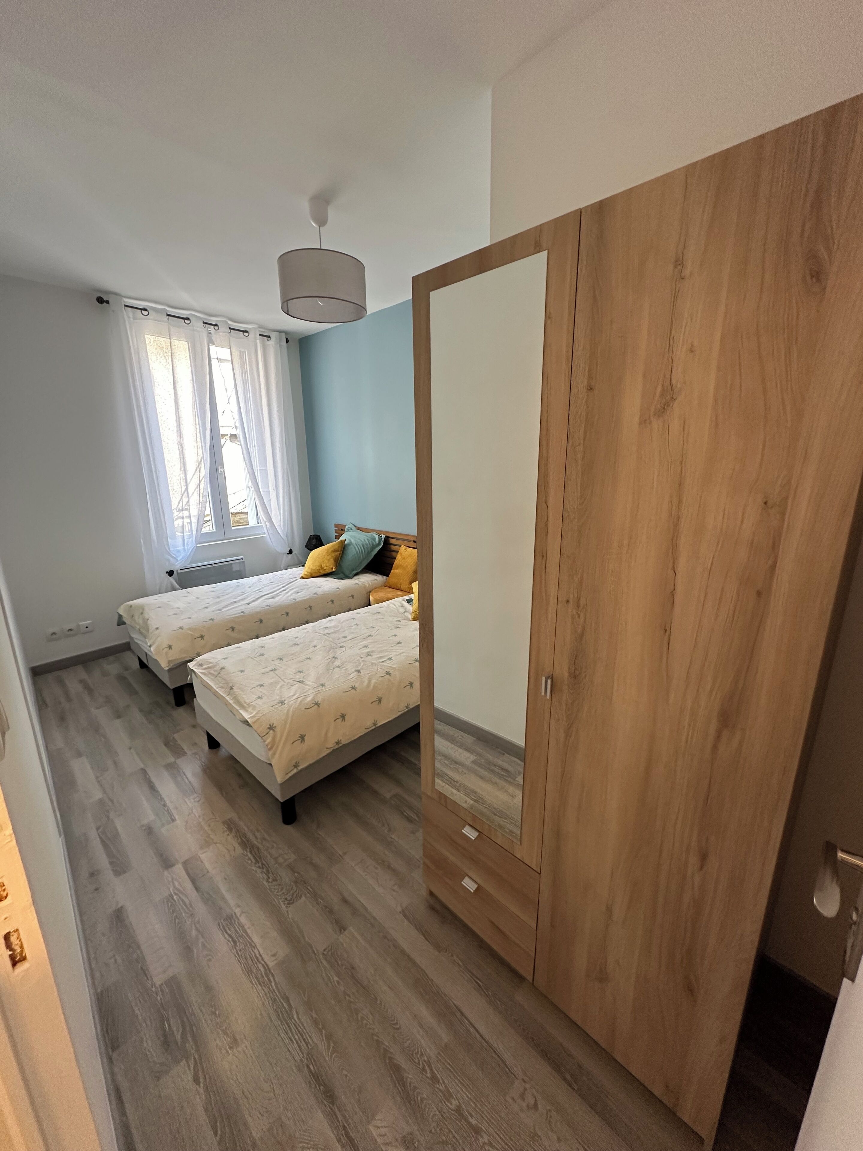 Un dormitorio con dos camas, un armario de madera y una ventana con cortinas.