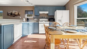 A modern kitchen with blue cabinets, a white refrigerator, and a dining table set for four. - Mountain Farm Stay, Alpacas & Views, Royal Gorge 15min (Cañon City)