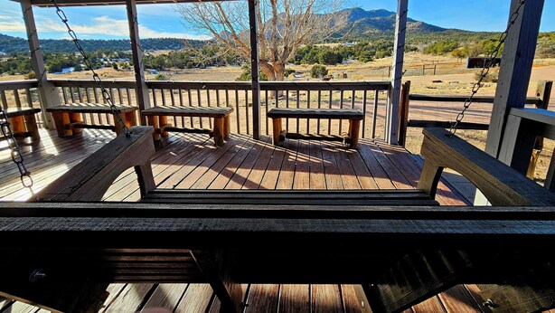 A wooden deck with benches and a swing, overlooking a rural landscape with mountains and trees. - Mountain Farm Stay, Alpacas & Views, Royal Gorge 15min (Cañon City)