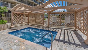 Un espace piscine agrémenté d’une pergola en bois, d’un panneau indiquant les règles du spa et d’un sauveteur en service.