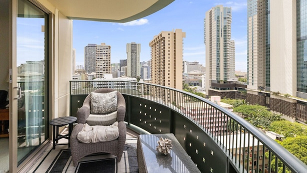 Un balcón con una silla y una mesa, vista del horizonte urbano y edificios altos.