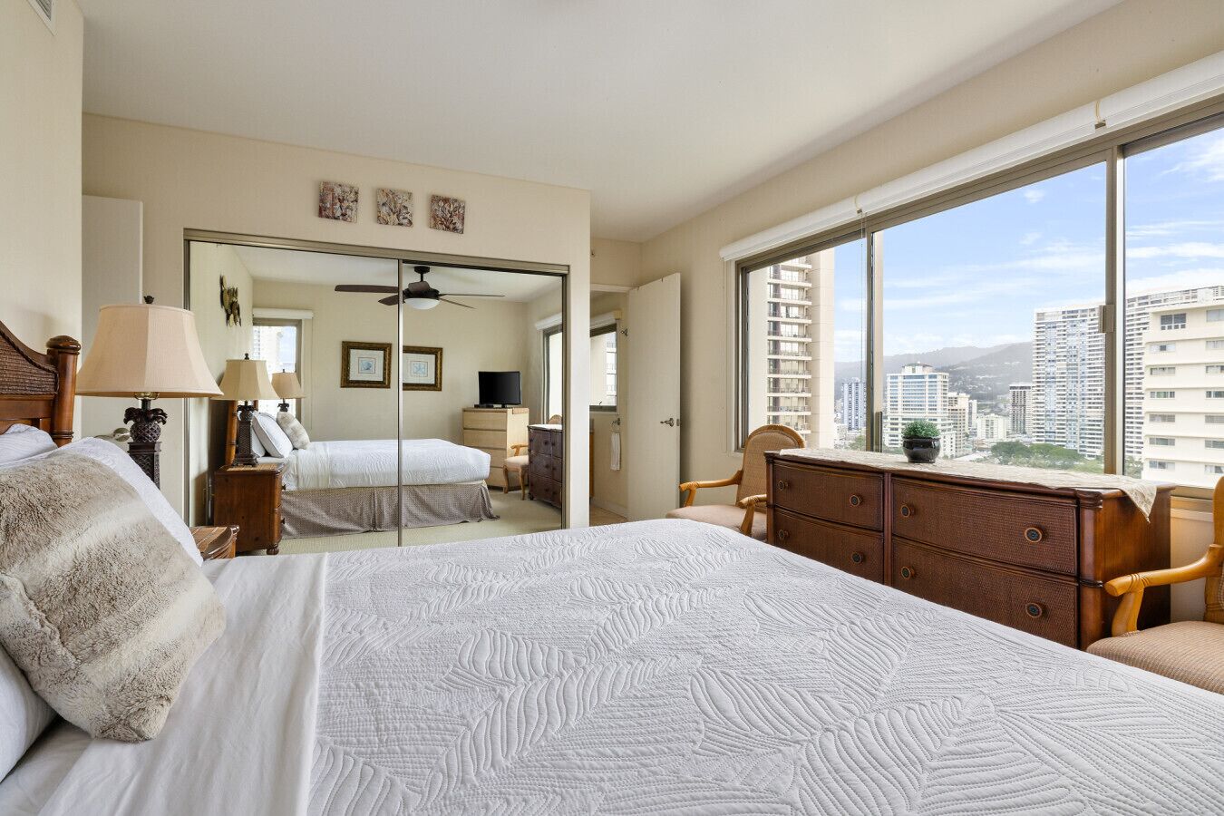 Hotelkamer met een groot bed, een dressoir, een stoel, een bureau, een spiegel en uitzicht op de stad.