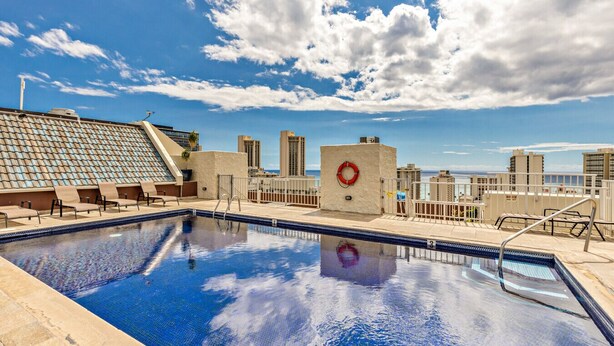 Une piscine sur le toit, équipée d’une bouée de sauvetage, de chaises longues et offrant une vue dégagée sur les toits de la ville.