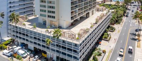 A multi-story hotel with a rooftop terrace, parking garage, and a street view with cars.