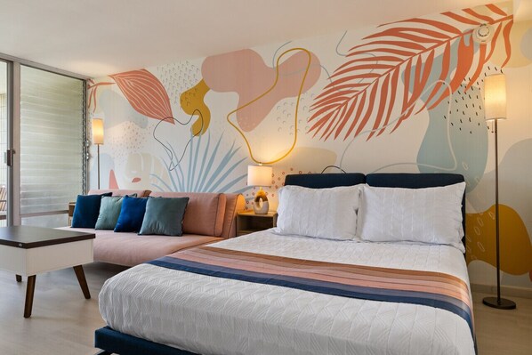 A modern hotel room with a large bed, a sofa, a desk, and a wall mural.