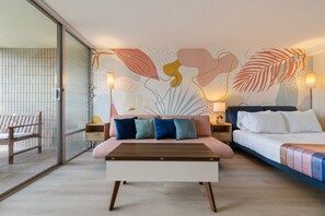 A modern bedroom with a sofa bed, a wooden coffee table, and a wall with abstract art. - Newly Renovated Pink Paradise Studio (Honolulu)