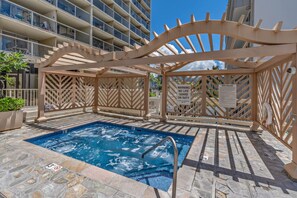 A pool area with a wooden pergola, a sign indicating spa rules, and a lifeguard on duty. - Waikiki Pink Paradise Studio | Lanai & Pool (Honolulu)