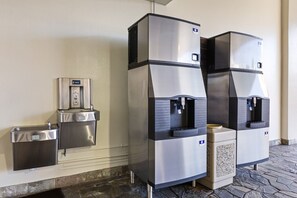 A water dispenser and trash bin mounted on a wall, with a stone-tiled floor. - Newly Renovated Pink Paradise Studio (Honolulu)