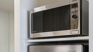 A compact kitchen with a stainless steel refrigerator and a microwave on top.