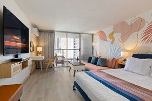 A modern hotel room with a large bed, a desk with a chair, a television, and a large window with a city view.