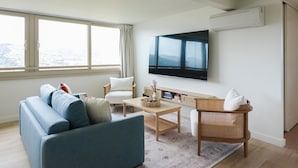 Ein modernes Wohnzimmer mit einem blauen Sofa, einem weißen Sessel, einem Couchtisch und einem an der Wand montierten Fernseher.