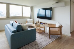 Una sala de estar moderna con un sofá azul, un sillón blanco, una mesa de centro y un televisor montado en la pared.