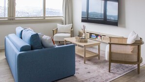 Ein modernes Wohnzimmer mit einem blauen Sofa, einem weißen Sessel, einem Holztisch und einem an der Wand montierten Fernseher.