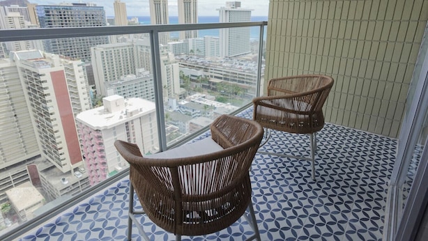 Ein Balkon mit zwei Korbstühlen, einem kleinen Tisch und fugenreichen Fliesen.