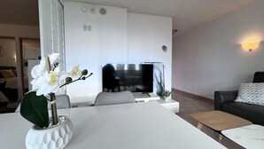 Un salon moderne avec un canapé blanc, une table basse et un téléviseur en arrière-plan.
