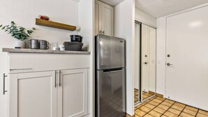 A compact kitchen with white cabinets, a stainless steel refrigerator, and a small countertop with kitchenware. - Island Style Studio Near the Shore! (Honolulu)