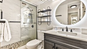 A modern bathroom with a glass shower enclosure, a white toilet, a vanity with a large mirror, and a towel rack. - Island Style Studio Near the Shore! (Honolulu)