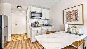 A compact kitchen with white cabinets, a microwave, and a dining area with a white table and chairs. - Island Style Studio Near the Shore! (Honolulu)