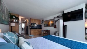 A hotel room with a bed, a desk, a kitchenette, and a TV.