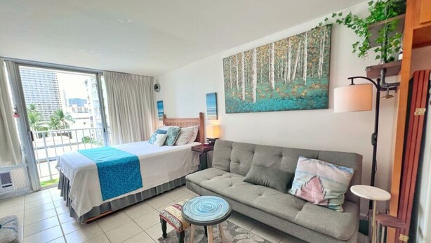 A hotel room with a bed, a sofa, a small round table, a lamp, and a painting on the wall.