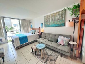A hotel room with a bed, a sofa, a small round table, a lamp, and a painting on the wall. - Waikiki Beach Studio: Walk 2 Surf + Assigned Prkng (Honolulu)