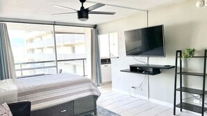Ein Hotelzimmer mit Bett, Wandfernseher, Deckenventilator und Blick auf den Balkon.