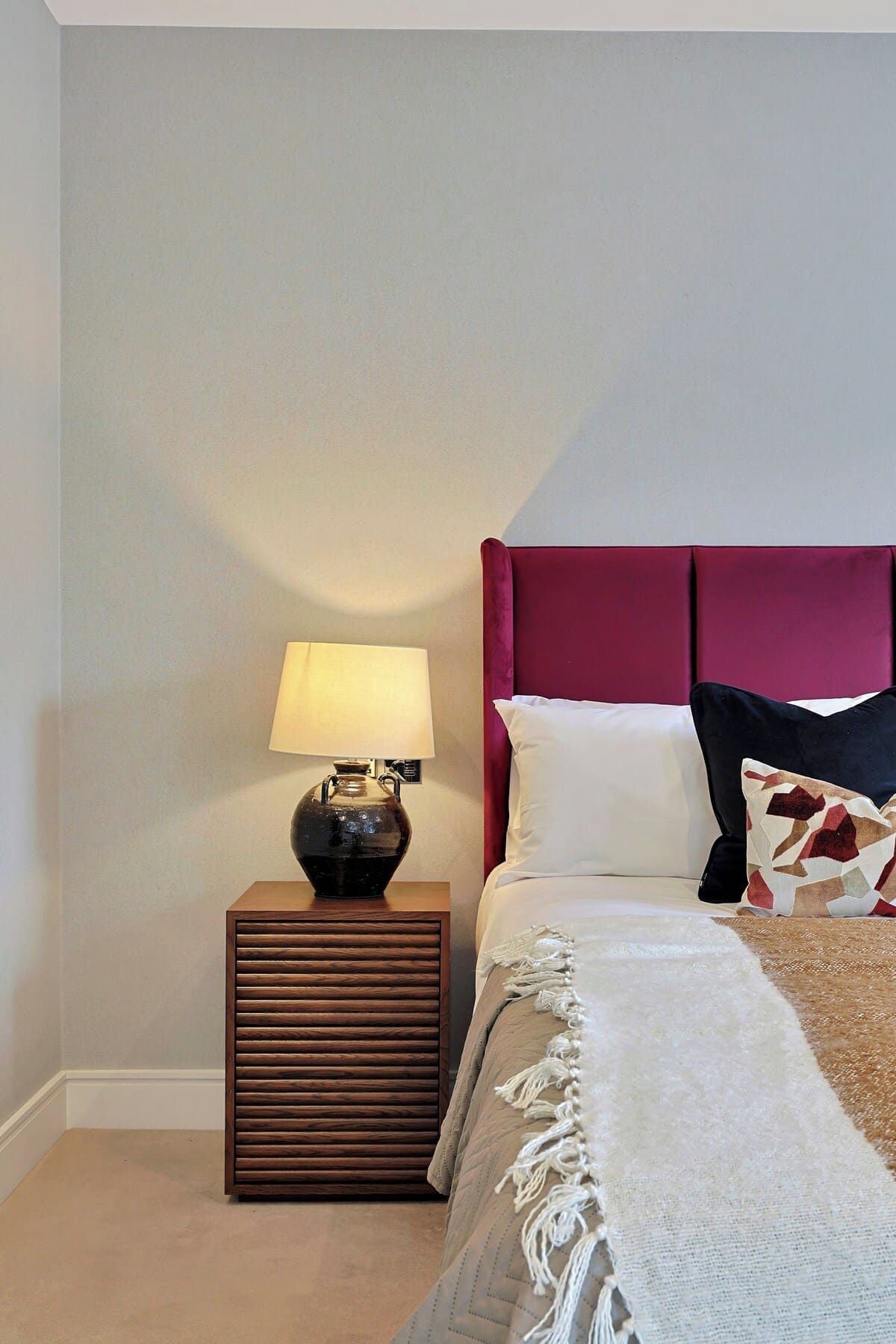 A bedroom with a bed, a nightstand with a lamp, and a wall-mounted light fixture.