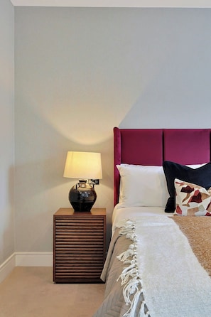 A bedroom with a bed, a nightstand with a lamp, and a wall-mounted light fixture.