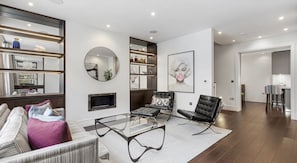 A modern living room with a glass coffee table, a black leather chair, and a sofa with patterned cushions.