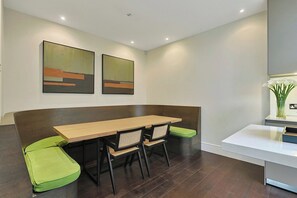 Een moderne eetruimte met een lange tafel, comfortabele zittingen en abstracte wanddecoratie.