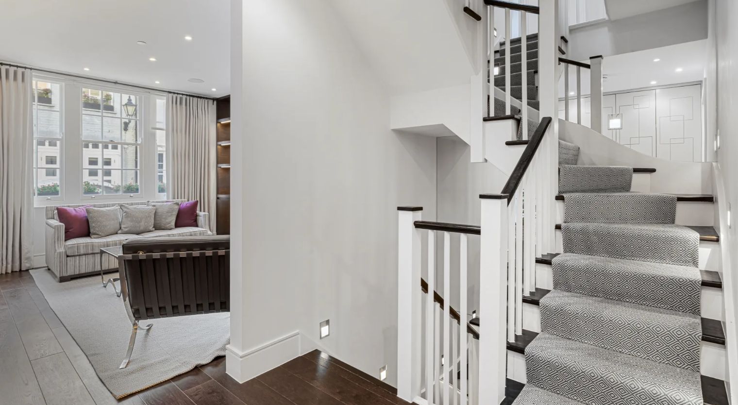 A modern staircase with a geometric patterned carpet, white walls, and a wooden handrail.