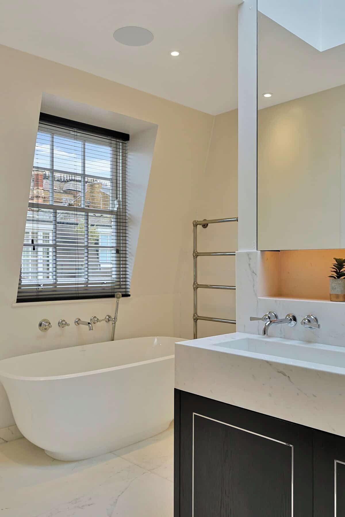 Une salle de bain moderne avec une baignoire sur pieds, un grand miroir et une fenêtre équipée de stores.