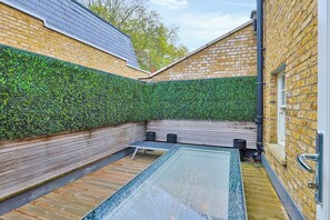 A modern outdoor pool area with a glass floor, surrounded by brick walls and wooden decking.