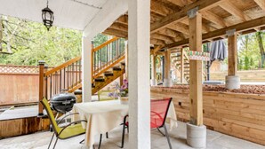 Ein überdachter Außenbereich mit Holzterrasse, Treppe, Grill und Tisch mit Stühlen.