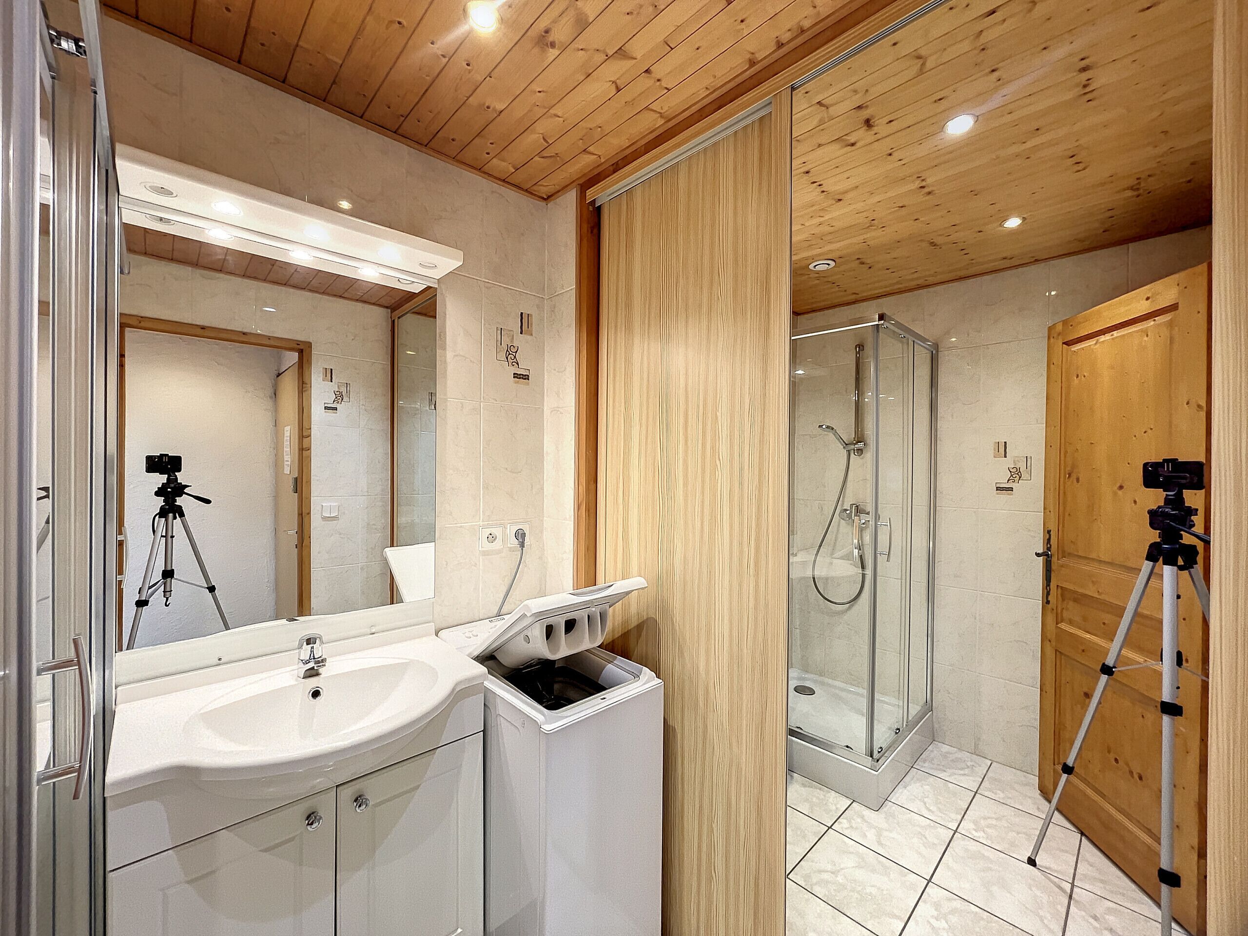 A modern bathroom with a wooden ceiling, a glass shower enclosure, and a sink with a mirror.
