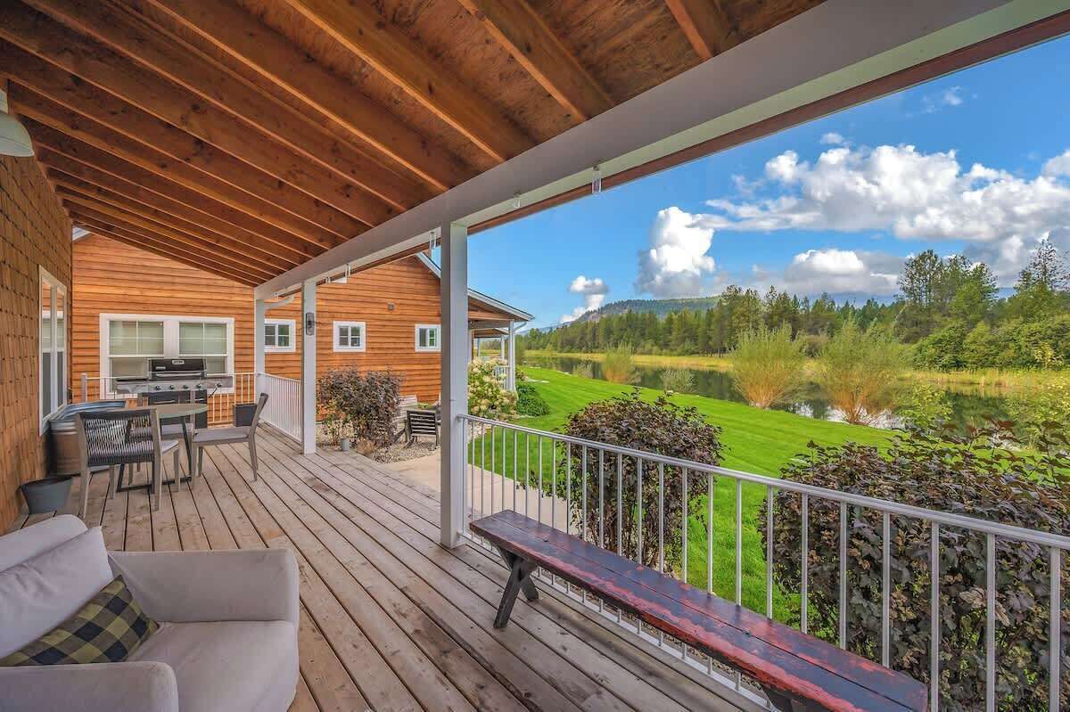 A wooden deck with outdoor furniture, a grill, and a view of a lake and forest.