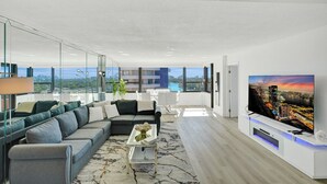 A modern living room with a large sofa, a coffee table, and a TV on a white stand. - Luxury Ocean View Condo / Beach Service / 1521 (Miami Beach)