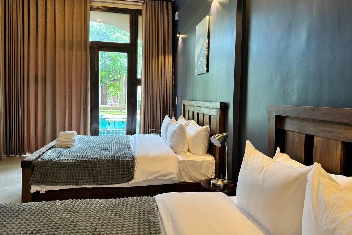 Camera d'albergo con due letti, un'ampia finestra e vista sul verde circostante.