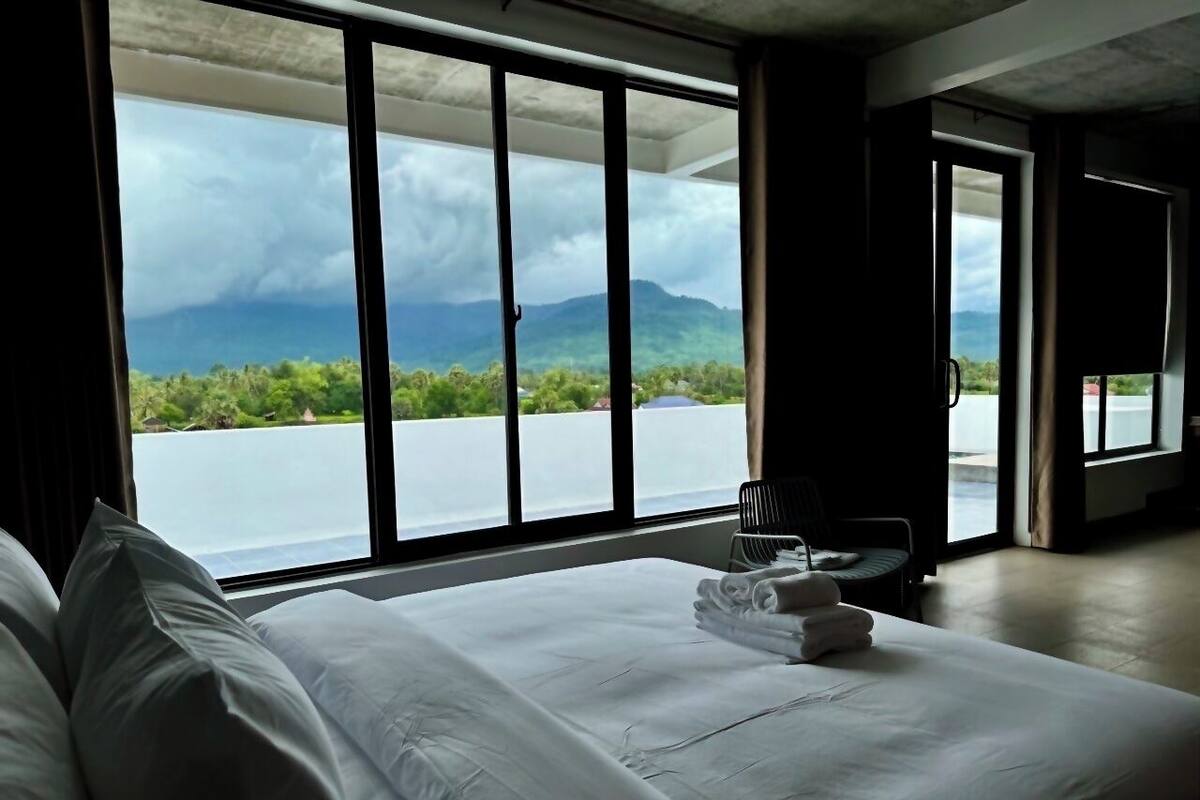 Camera d'albergo con un letto grande, una sedia e vista su un lago e montagne.