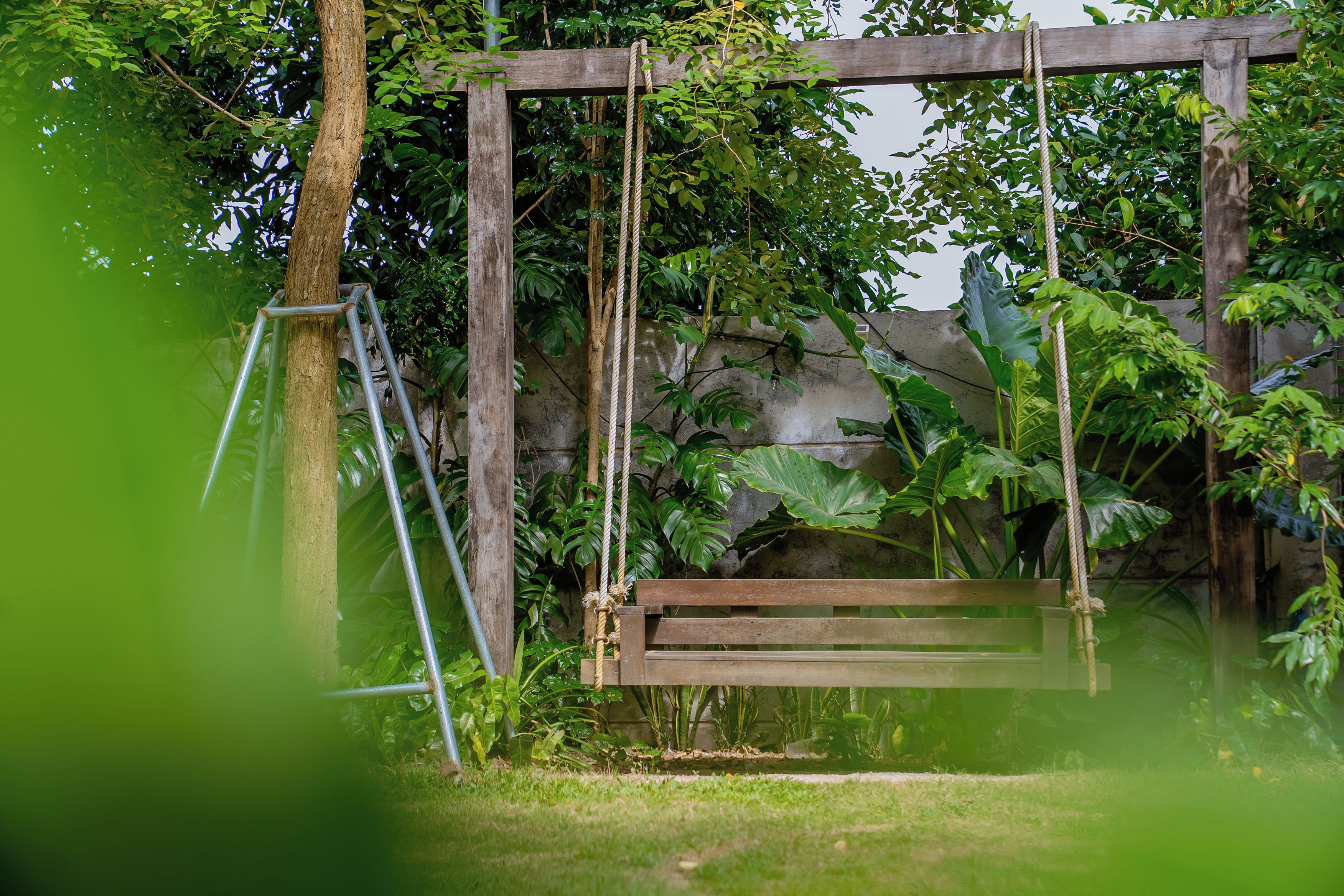 A wooden swing set in a garden with a stone wall and lush greenery.