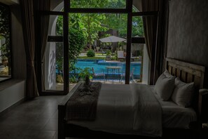 A bedroom with a large window overlooking a swimming pool and garden. - Stone Age Boutique  (Kampot)