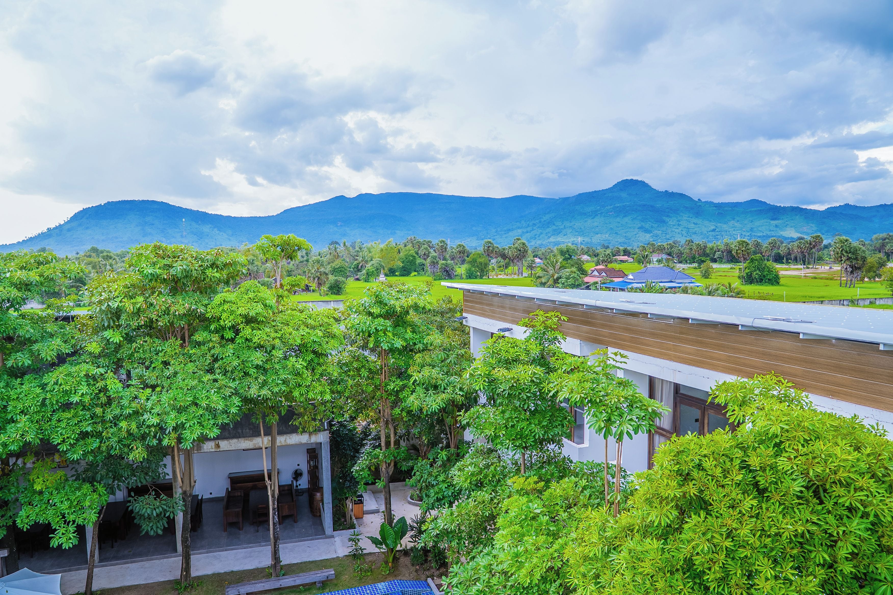 A modern building with a flat roof, surrounded by lush greenery and a mountainous backdrop.
