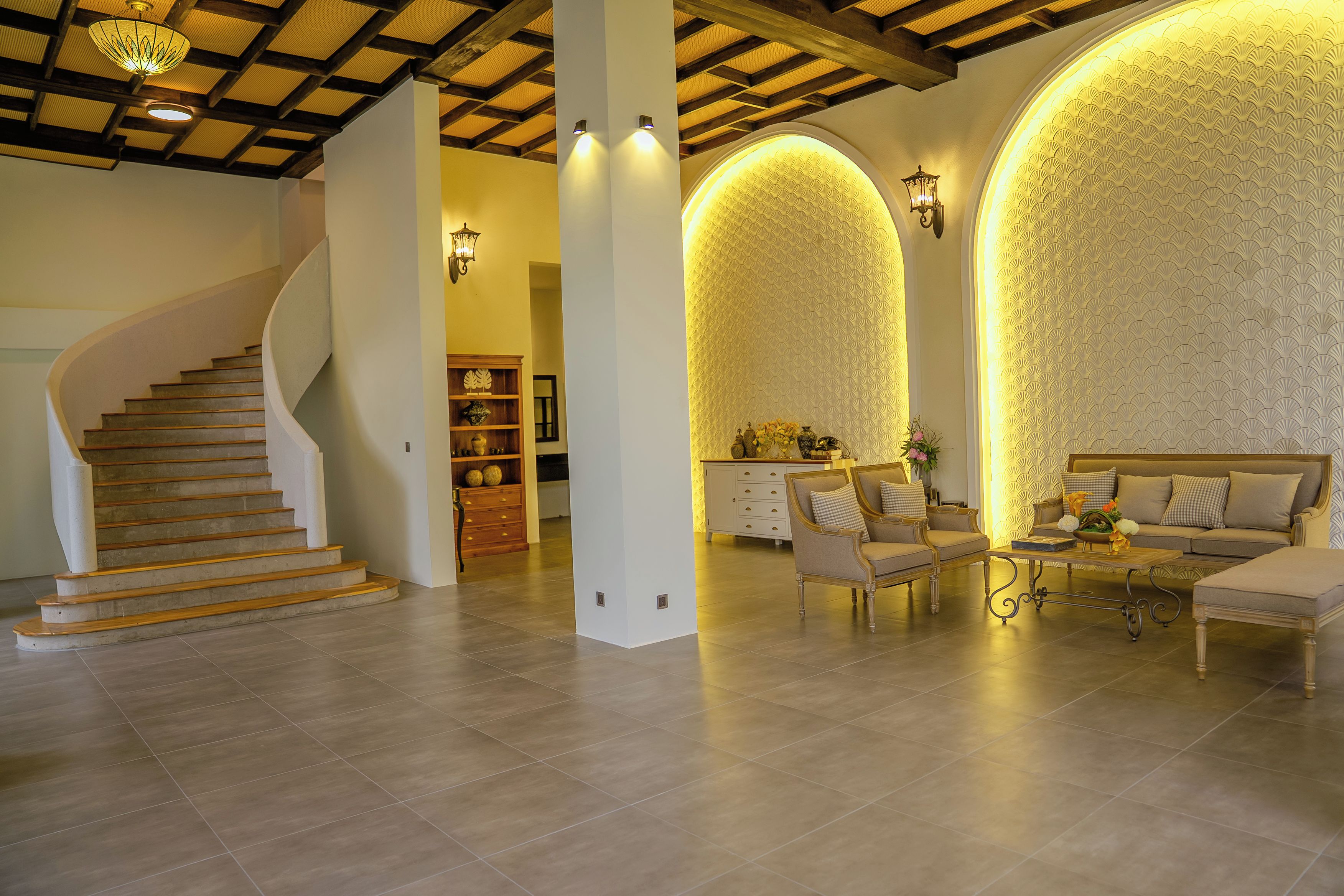 A spacious living area with a curved staircase, a sofa set, and a decorative wall with a scalloped pattern.