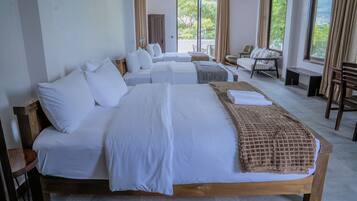 A hotel room with a large bed, multiple pillows, a bedside table, a chair, and a view of greenery outside.